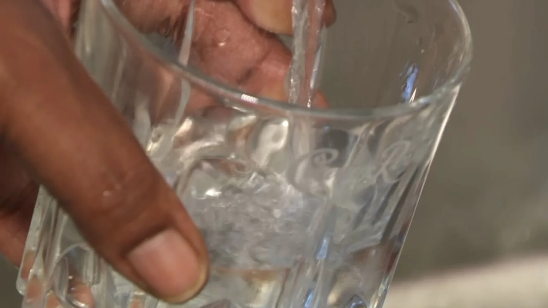 an image of tap water being drawn from a sink into a glass. a person is holding the glass under the faucet.