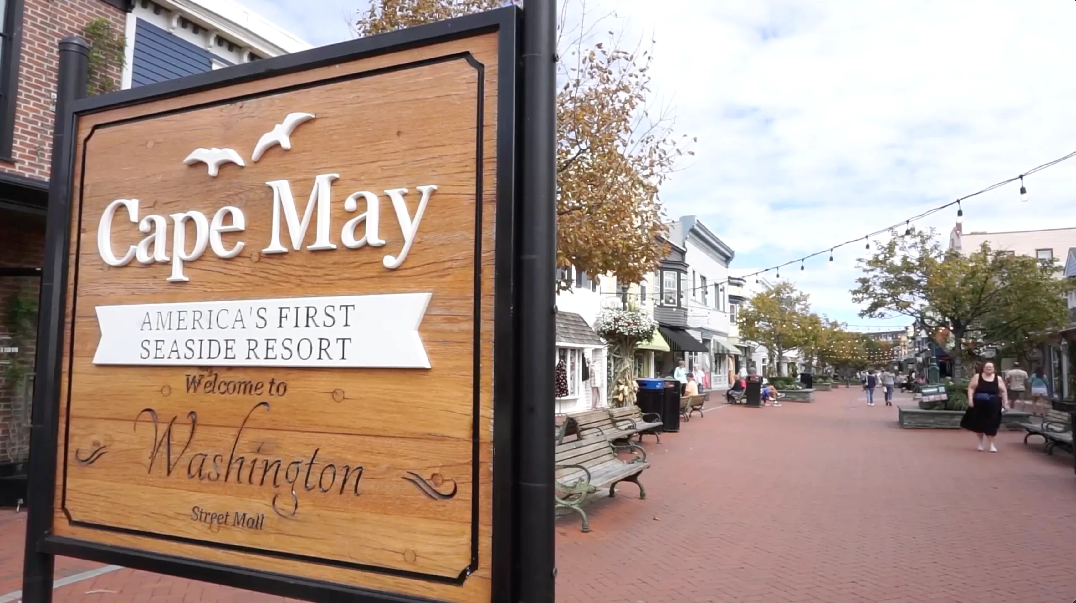a sign that says Cape May in front of a downtown pedestrian area.
